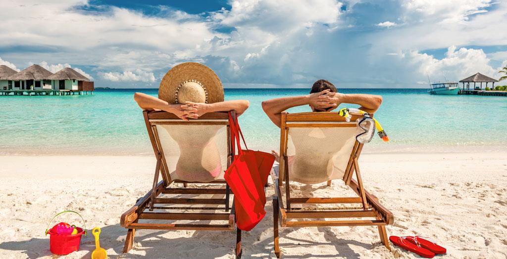 Paar entspannt am türkisfarbenen Meer auf Sonnenstühlen