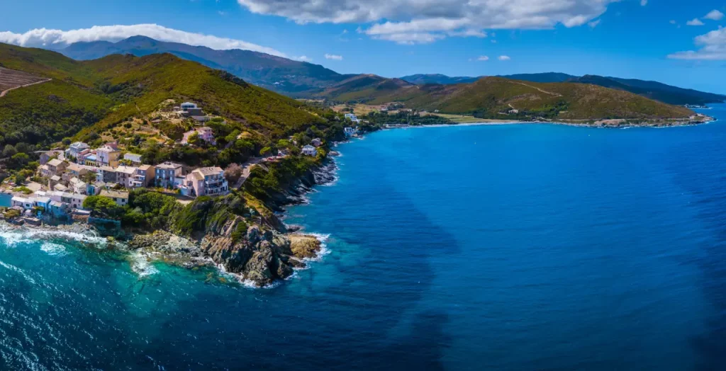Kleines Dorf am Meer auf Korsika, Frankreich, mit türkisblauem Wasser und grünen Hügeln