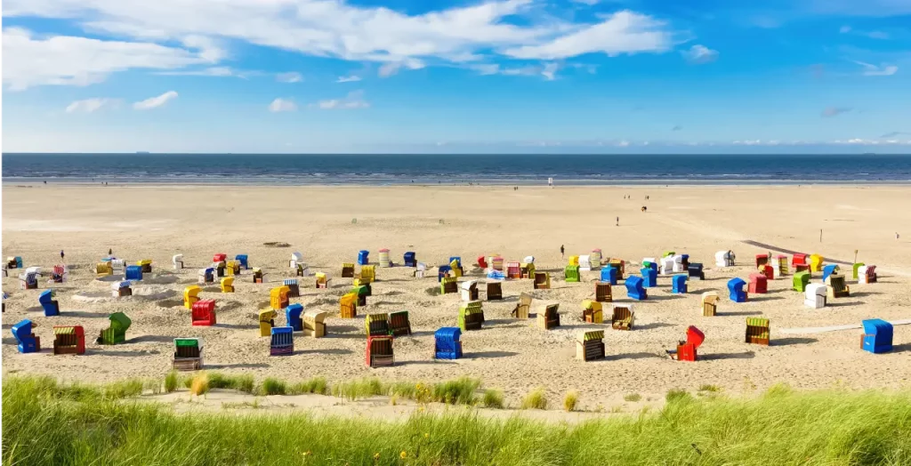 Farbenfrohe Strandkörbe am Sandstrand von Juist, Nordseeinsel Deutschland, mit Dünen im Vordergrund und blauem Himmel