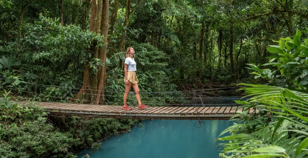 Junge Frau wandert im tropischen Regenwald und geht auf einer Brücke über die türkisfarbene Lagune von Costa Rica