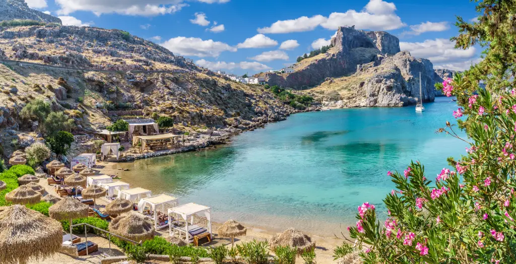Strand und Bucht 
 von Saint Paul auf der Insel Rhodos in Griechenland, mit türkisfarbenem Wasser und Oleanderblüten