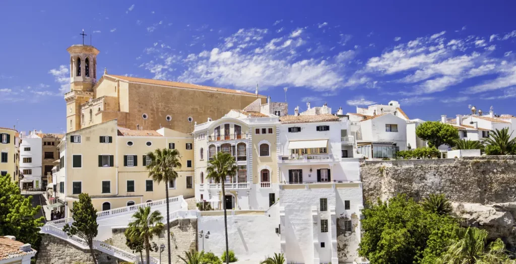 Historische Architektur der alten Stadt Mahon auf Menorca mit charakteristischen Gebäuden und Kirchturm unter blauem Himmel