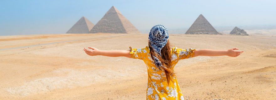Frau mit Rücken zum Betrachter gewandt in Wüste Ägyptens mit Pyramiden im Hintergrund