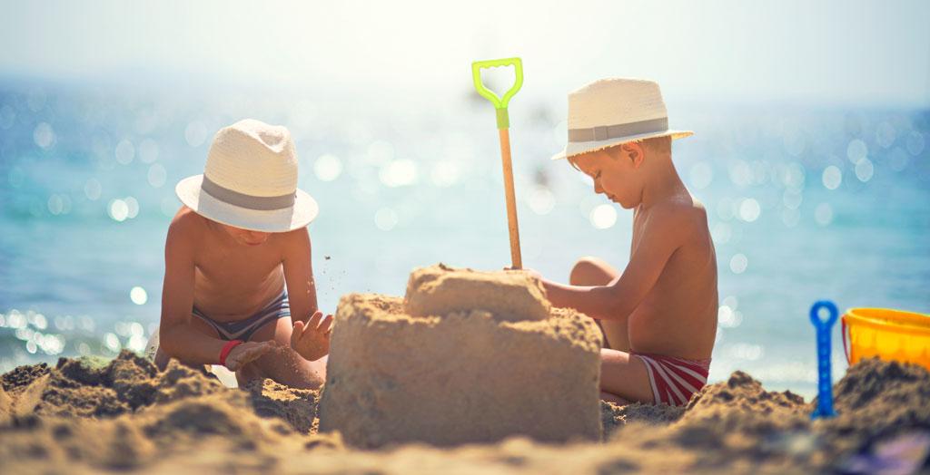 Zwei Kinder mit Hüten bauen eine Sandburg am Strand