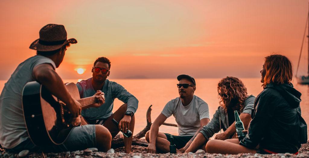 Freunde spielen gemeinsam Gitarre und entspannen am Strand von Kroatien