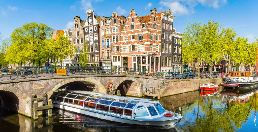 Sightseeing-Boot fährt unter einer Brücke im Kanal Amsterdams mit historischen Häusern im Hintergrund