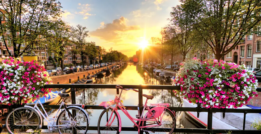 Sonnenuntergang über einer Amsterdamer Gracht mit einem weiß und einem pinkfarbenen Fahrrad an der Brücke