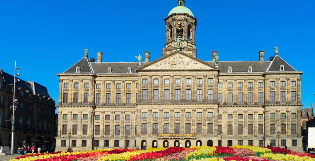 Königspalast in Amsterdam umgeben von farbenprächtigen Blumenbeeten unter blauem Himmel