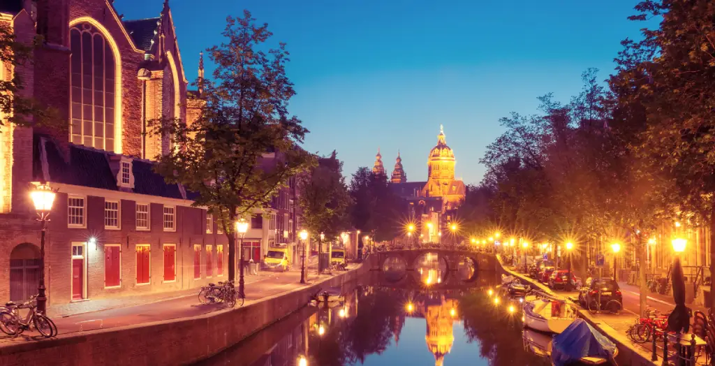 Beleuchtete Abendansicht des Rotlichtviertels De Wallen in Amsterdam mit Spiegelung der Lichter im Kanal