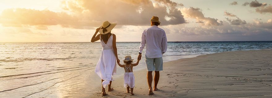 Familie mit Kind spaziert zum Sonnenuntergang am Strand entlang