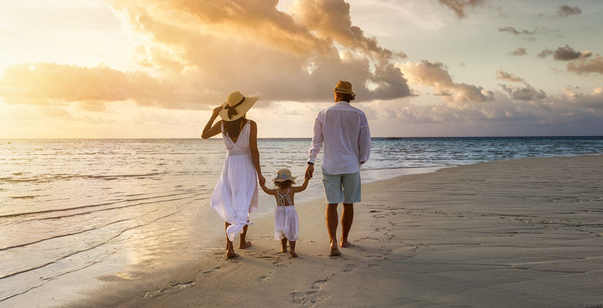 Familie mit Kind spaziert zum Sonnenuntergang am Strand entlang
