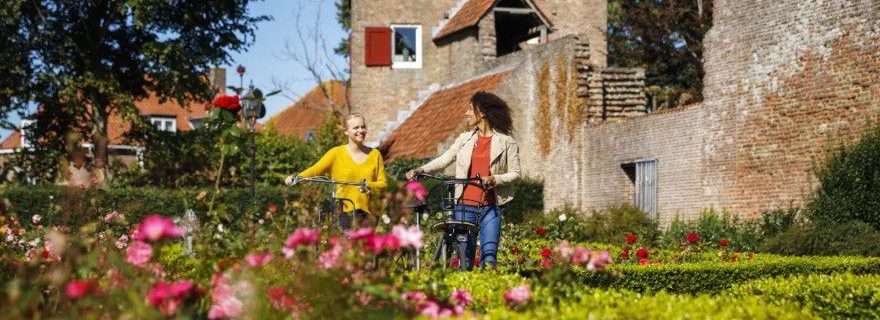 2 Frauen laufen mit dem Fahrrad durch die Natur in Harderwijk. Links im Bild befindet sich ein Strauch mit rosafarbenen Blüten