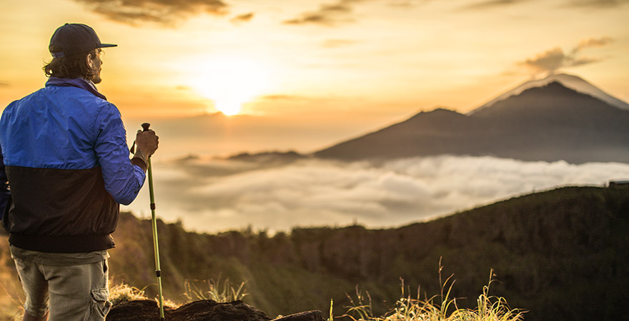 Mann steht auf einem Berg und schaut auf den Sonnenaufgang