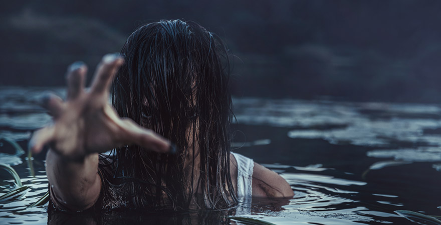 Gruselige Frau die im Wasser ist deren Haare über das Gesicht hängen und die eine Hand ausstreckt