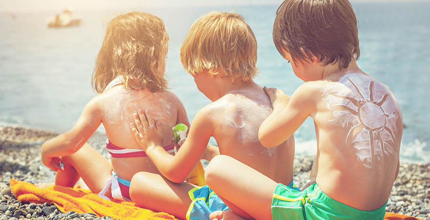 3 Kinder cremen sich mit Sonnencreme ein