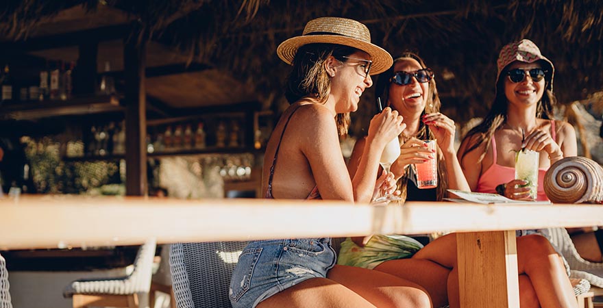 Drei Frauen mit Cocktails an einer Strandbar auf Mykonos