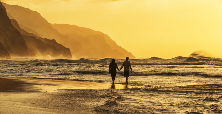 Paar beim Spaziergang am Strand bei Sonnenuntergang auf Hawaii