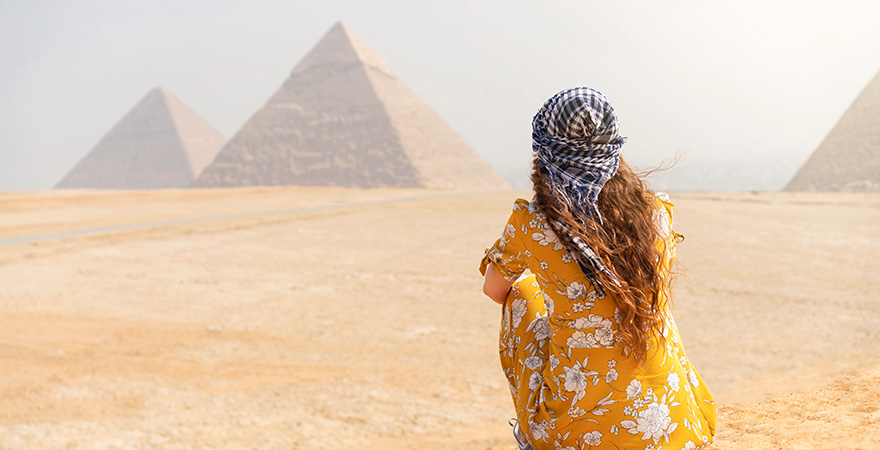Frau sitzt im Sand und blickt auf die Pyramiden von Gizeh in Ägypten