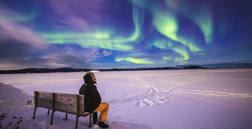 Mann sitzt auf einer Bank und schaut die Polarlichter in Finnland an