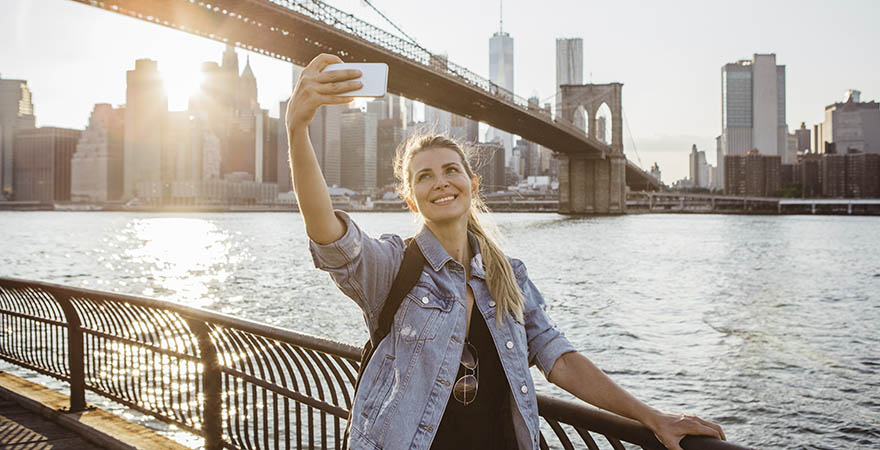 Frau macht ein Selfie vor der Brooklyn Bridge und Skyline von New York