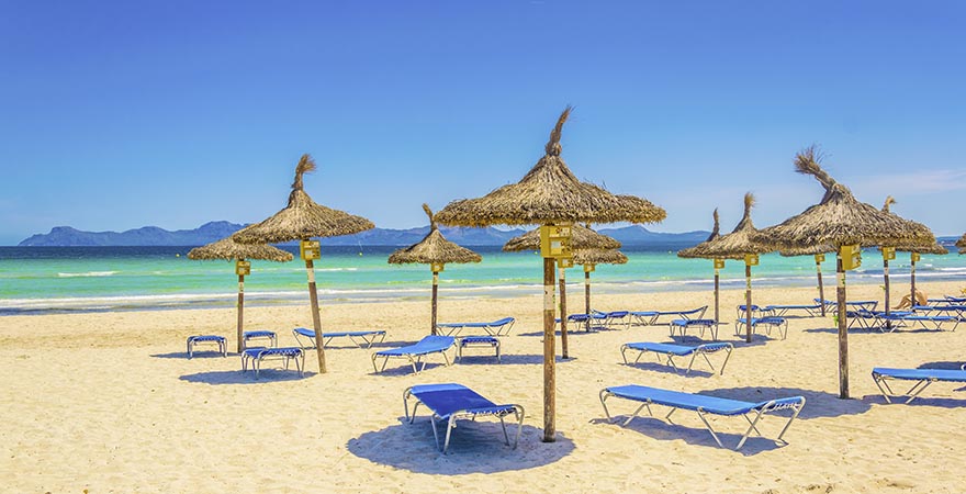 Strand mit strohgedeckten Sonnenschirmen vor einem türkisfarbenen Meer