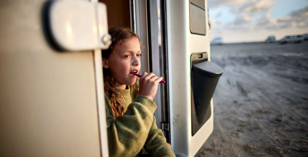 Mädchen putzt beim Camping ihre Zähne vor dem Wohnwagen