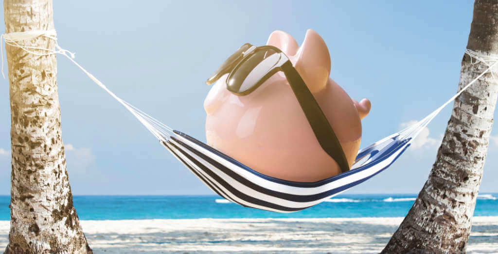 Pinkes Sparschwein mit Sonnenbrille entspannt in einer Hängematte am Strand