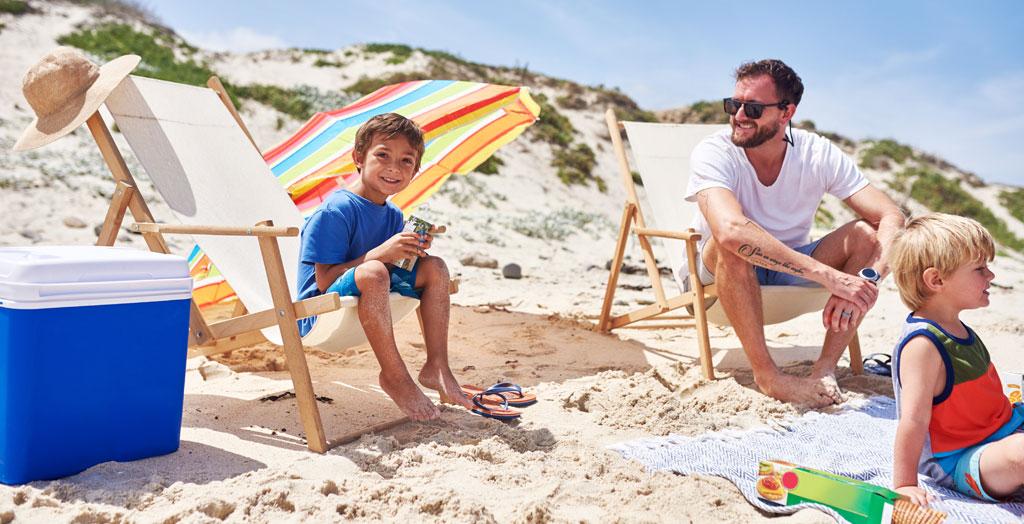 Porträt eines Vaters der mit seinen Kindern am Strand ein Picknick genießt