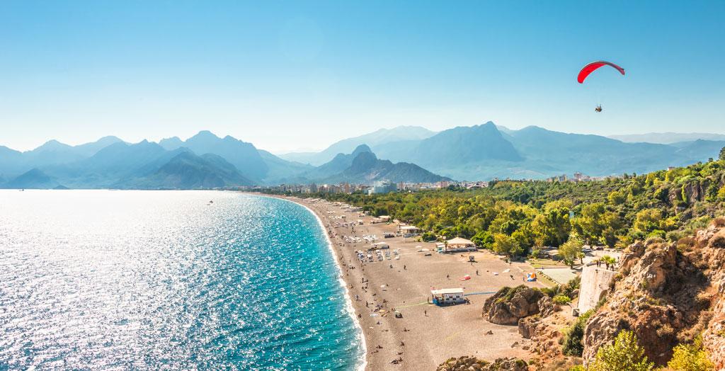 Gleitschirmflieger über der glitzernden Küste von Antalya mit Bergpanorama im Hintergrund, Türkei