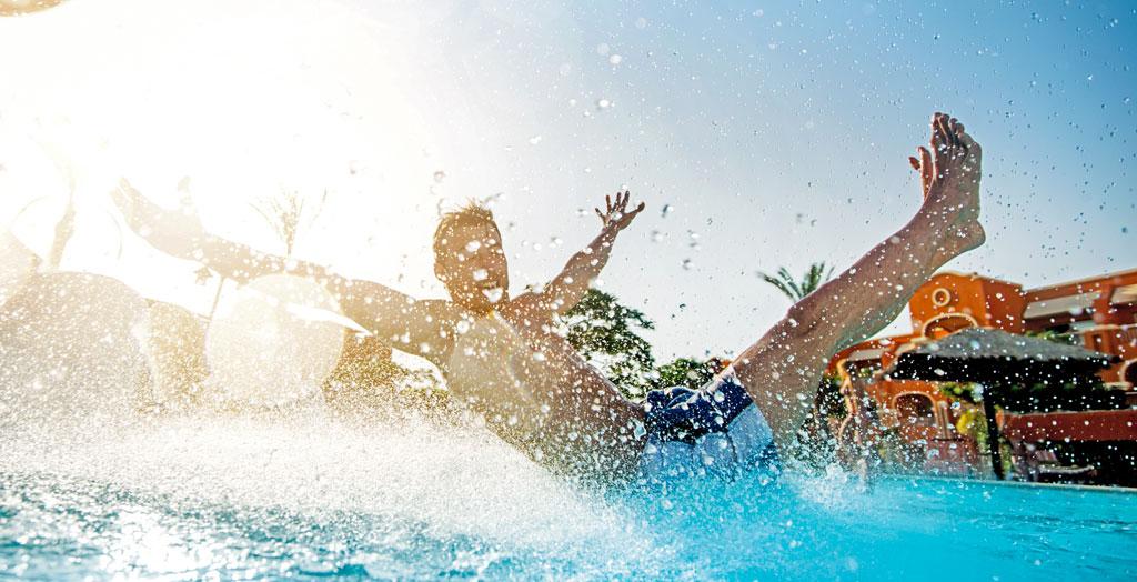 Mann genießt eine aufregende Fahrt auf einer Wasserrutsche in einem Aquapark, umgeben von spritzendem Wasser und strahlendem Sonnenschein