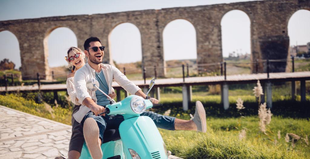 Junges Paar im Sommerurlaub haben Spaß beim Fahren eines Oldtimer-Rollers am antiken Stein-Aquädukt-Denkmal