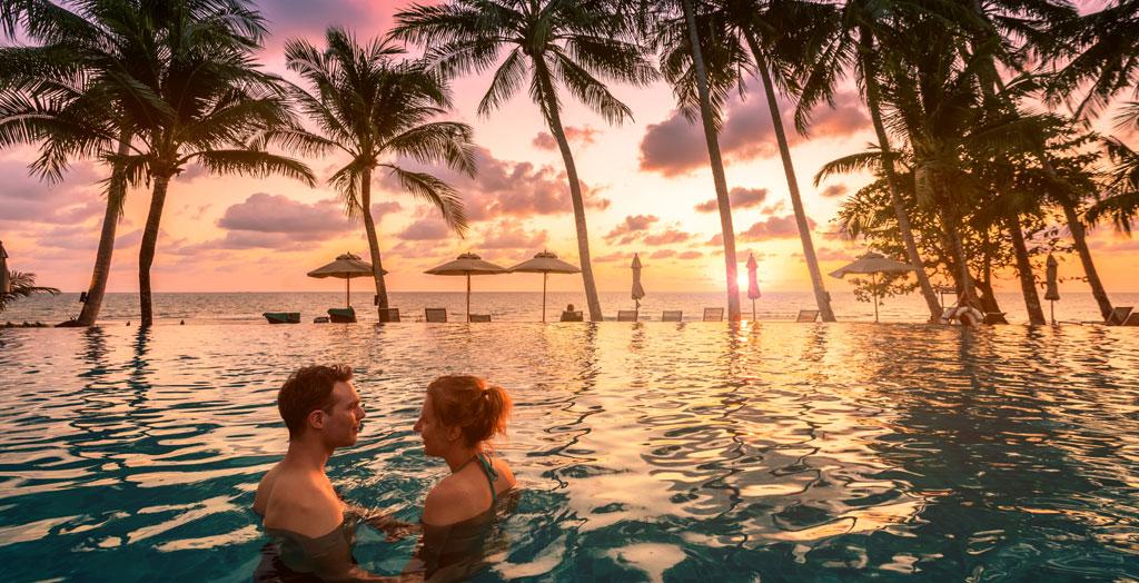 Paar im Strandurlaubsort entspannt sich im Schwimmbad mit malerischer tropischer Landschaft bei Sonnenuntergang in Thailad