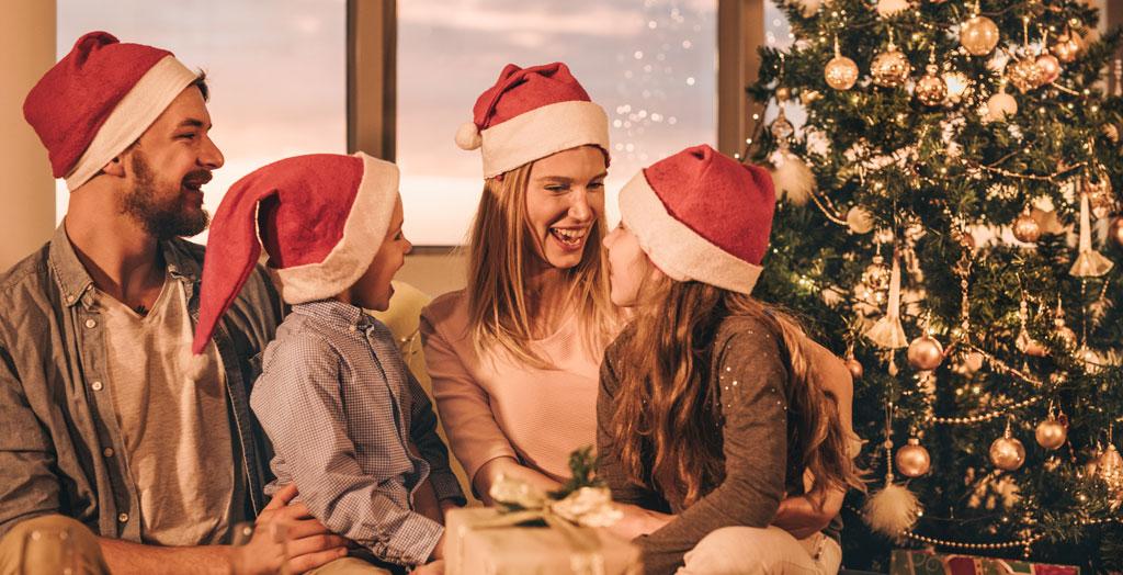 Glückliche Eltern verbringen Weihnachten mit ihren kleinen Kindern neben dem Tannenbaum 