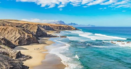 Blick auf die Playa del Viejo Rey mit markanten Felsformationen und Surfern an der Küste Fuerteventuras, Kanarische Inseln, Spanien