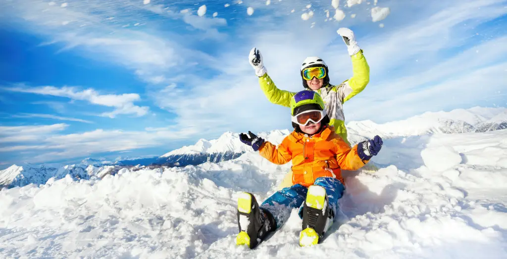 Frau und Kind sitzen im Schnee und werfen einen Schneeball