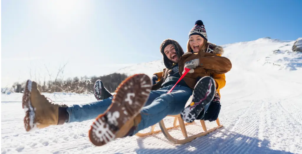 Junges verliebtes Paar beim Schlittenfahren hat Spaß im Schnee