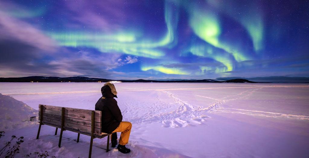Mann auf einer Bank schaut sich Polarlichter - Nordlichter an
