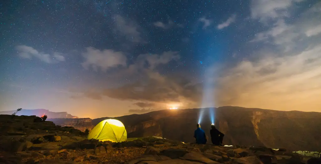 Zwei Männer blicken vom Wüstenlager aus in den Nachthimmel mit Sternen in Oman