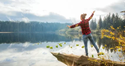 Junge Frau balanciert auf einem Baumstamm über dem See, Vancouver Island in British Columbia, Kanada