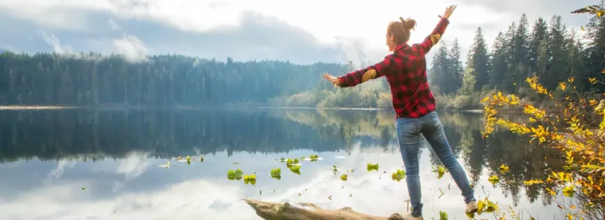 Frau balanciert über einen Baumstamm über dem See auf Vancouver Island, British Columbia