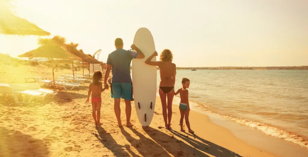 Familie mit Surfboard spaziert am Strand entlang [Bildquelle: © valentinrussanov | Canva]