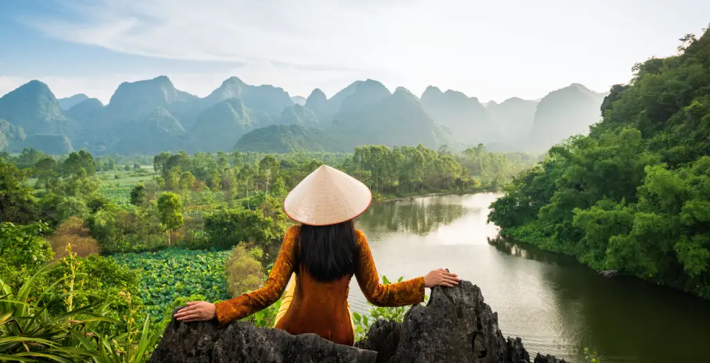 Frau in traditioneller Kleidung sitzt auf einem Hügel und blickt auf die Berge und den Fluss namens Parfüm, Vietnam