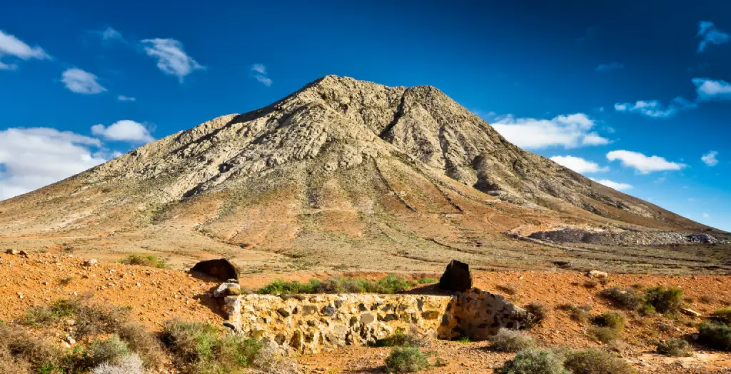 Der heilige Berg Tindaya ragt in die Höhe, umgeben von der kargen Landschaft Fuerteventuras, Kanarische Inseln, Spanien. [Bildquelle: © fotofly1960 | Canva]
