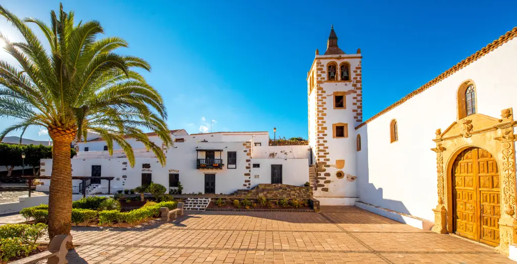 Historische Kirche im malerischen Betancuria-Dorf auf Fuerteventura, Kanaren, Spanien, umgeben von Palmen und traditionellen weißen Gebäuden