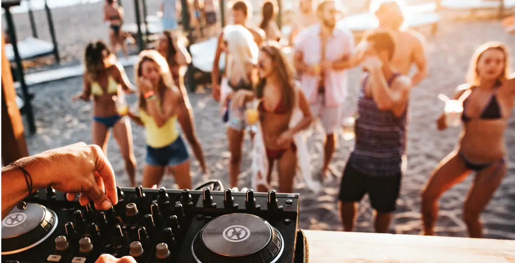 DJ legt Musik auf einer lebendigen Strandparty auf, während tanzende Menschen im Hintergrund das Fest genießen