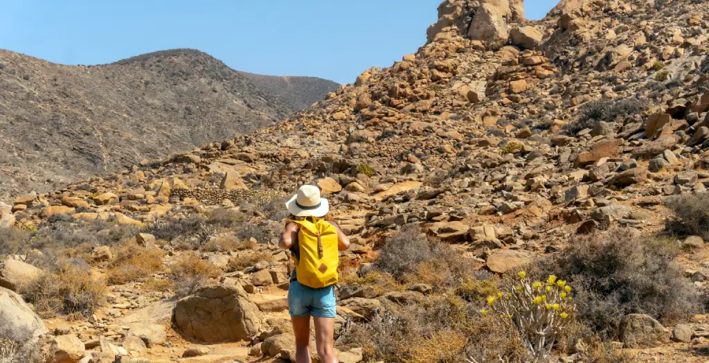 Frau wandert auf dem Mirador de la Peñitas Trail im Peñitas Canyon auf Fuerteventura, umgeben von rauen Felsformationen und einheimischer Vegetation. [Bildquelle: © Wirestock  | Canva]