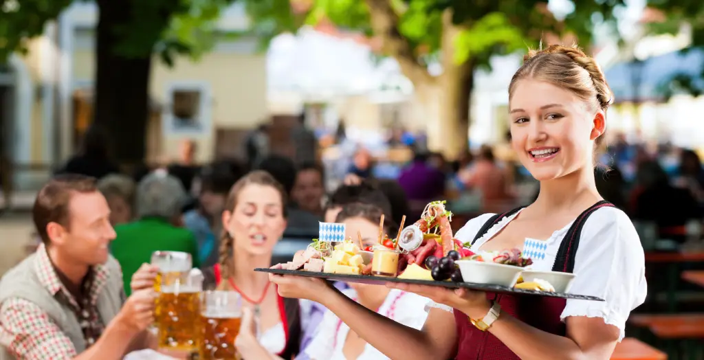 Kellnerin im bayerischen Dirndl serviert regionale Köstlichkeiten in einem Biergarten in Bayern, Deutschland
