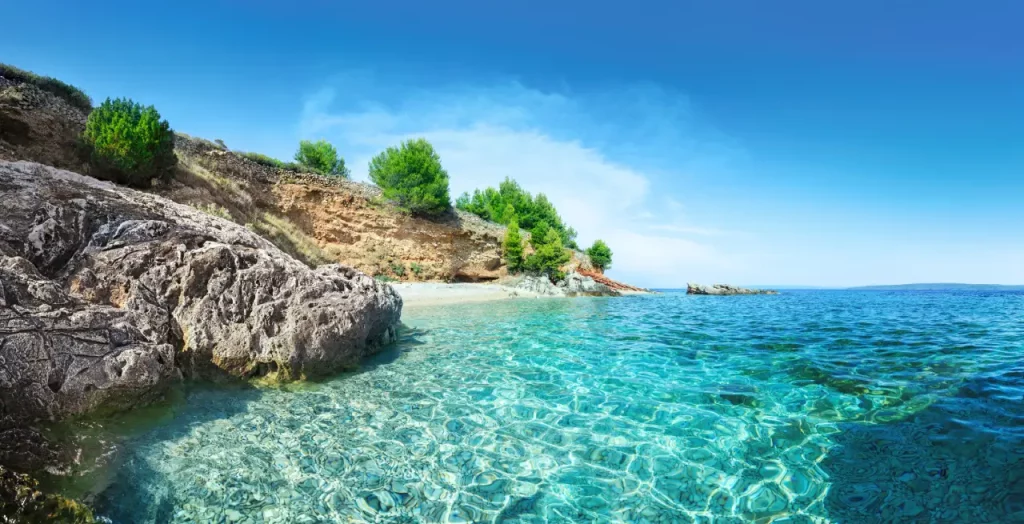 Kristallklares Wasser in einer ruhigen Bucht auf Hvar, Kroatien, mit felsiger Küste und grüner Vegetation