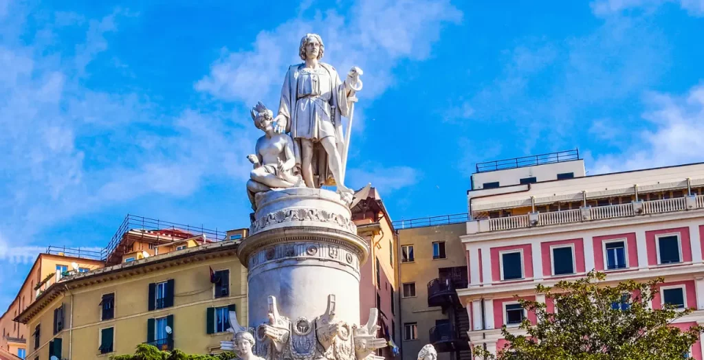 Das Denkmal von Christoph Kolumbus in Genua, Italien, mit Himmel im Hintergrund und umgeben von städtischer Bebauung [Bildquelle: © claudiodivizia | Canva]