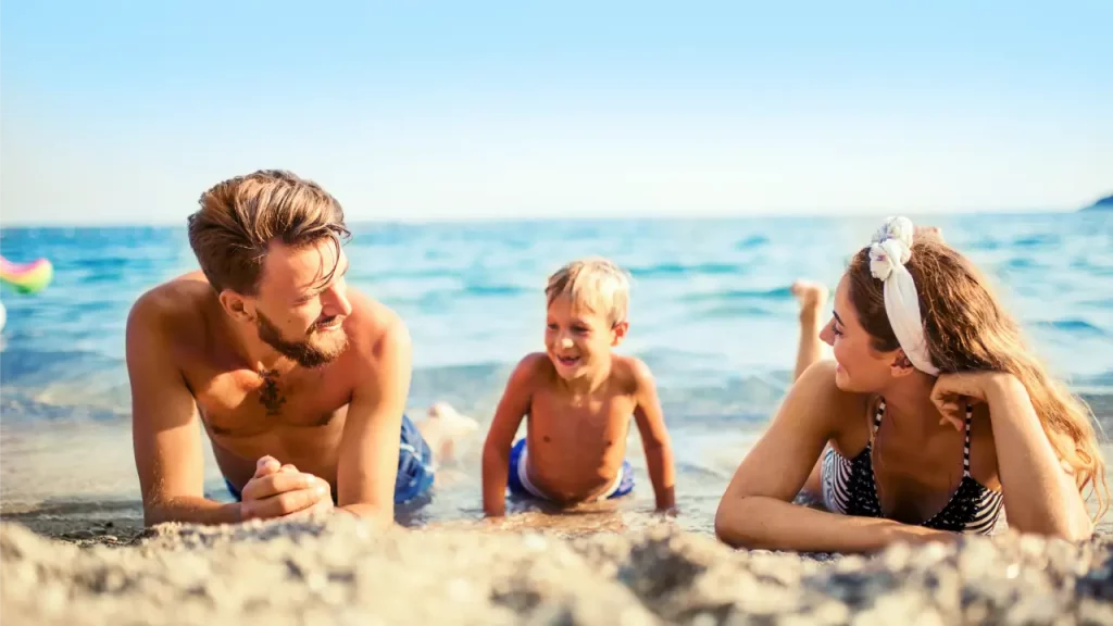 Familie entspannt lachend am sonnigen Strand in Montenegro, mit kristallklarem Meer im Hintergrund